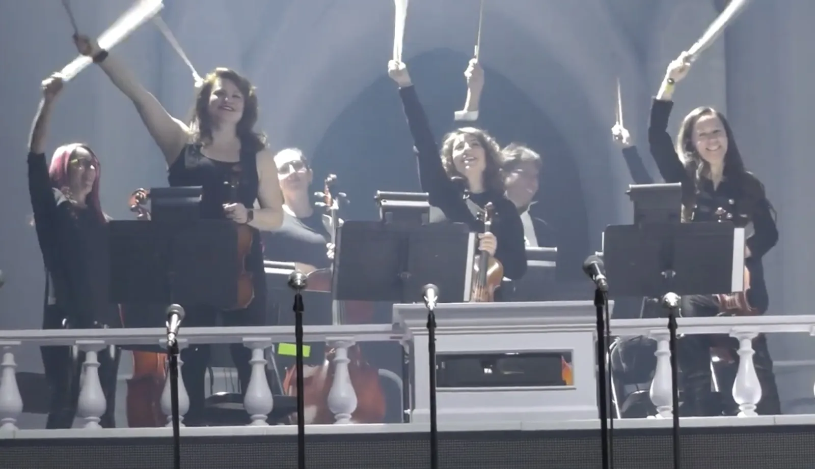String section on a large arena stage under white beams of light