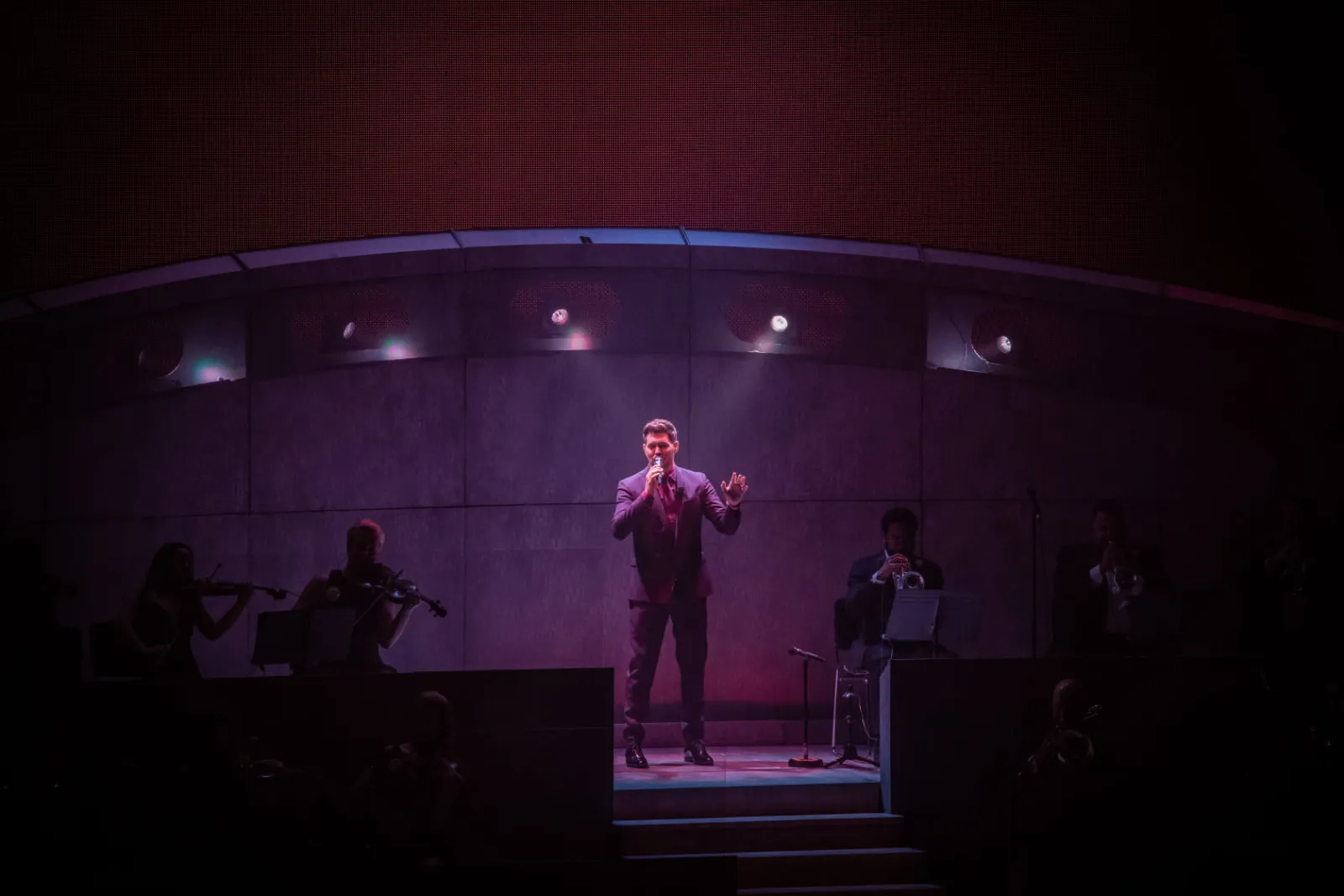 Ashley playing electric violin in a pink spotlight on a dark stage