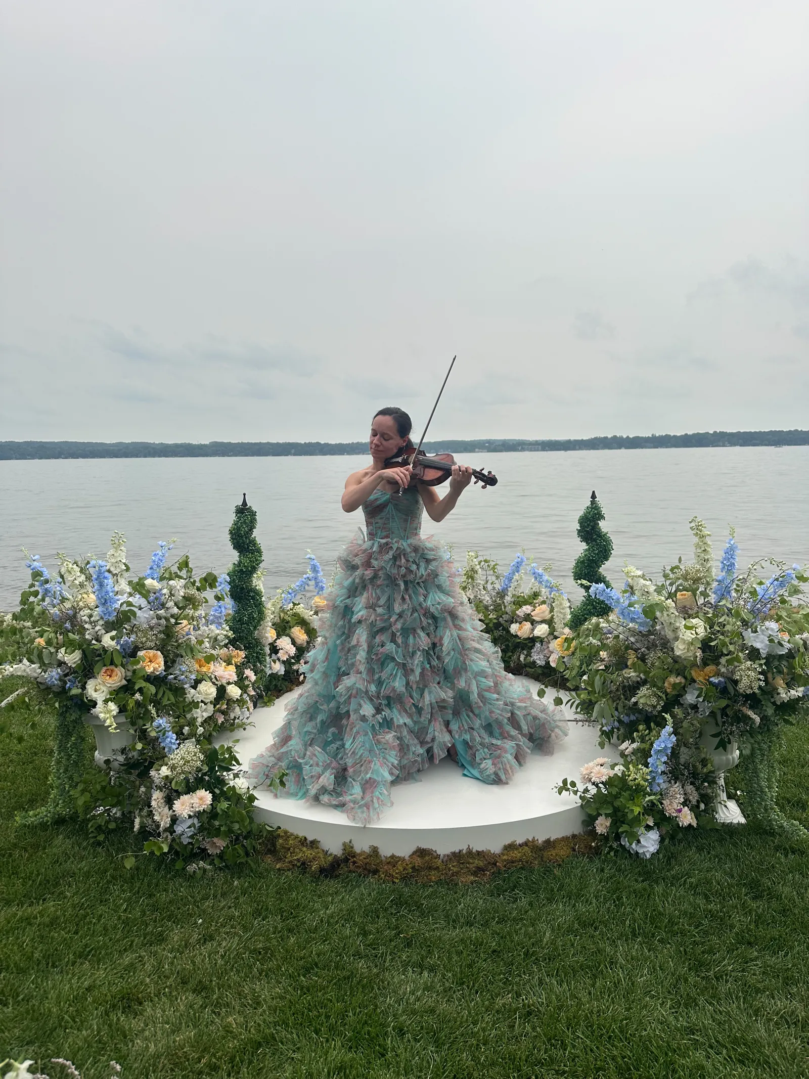 Ashley playing acoustic violin in a ball gown at a lakeside wedding